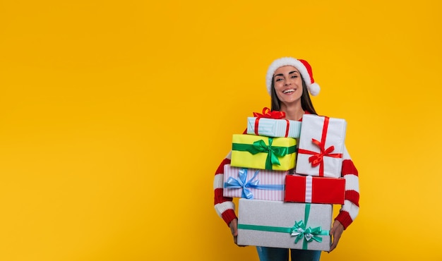 Glückliche wunderschöne Frau mit vielen Weihnachts- und Neujahrsgeschenken in den Händen posiert auf gelbem Hintergrund