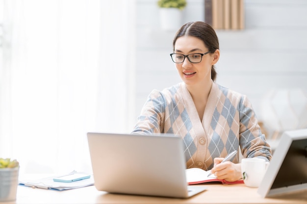 Glückliche zufällige schöne Frau, die zu Hause an einem Laptop arbeitet.