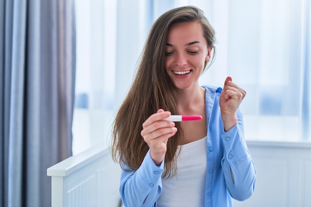 Glückliche zufriedene freudige Frau freut sich über ein positives Schwangerschaftstestergebnis. Geplante und lang erwartete gewünschte Schwangerschaft