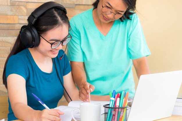 Glückliche zwei asiatische Mutter ist eine Lehrerin, die ihrer Tochter ein Online-Studium von der Schule mit einem Laptop-Computer aus der Universitätsklasse gibt, die von zu Hause aus lernt