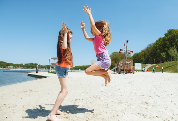 Glückliche zwei kleine Mädchen haben Spaß und rennen fröhlich am Strand, springen auf den Sand