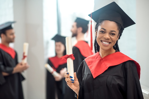 Glücklicher Absolvent. Nettes afroamerikanisches Mädchen im Mortarboard, das glücklich schaut und schön lächelt