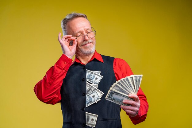 Glücklicher älterer Geschäftsmann mit Fan von Dollarscheinen, die auf gelbem Hintergrund isoliert sind