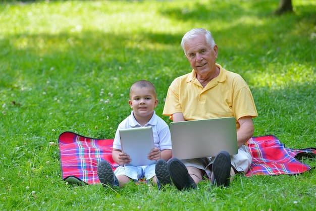 glücklicher älterer Großvater und Kind im Park mit Laptop-Computer