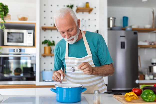 Glücklicher älterer Mann, der Spaß beim Kochen zu Hause hat Ältere Person, die ein gesundes Mittagessen in der modernen Küche zubereitet Retired Lifestyle Time and Food Nutrition Concept