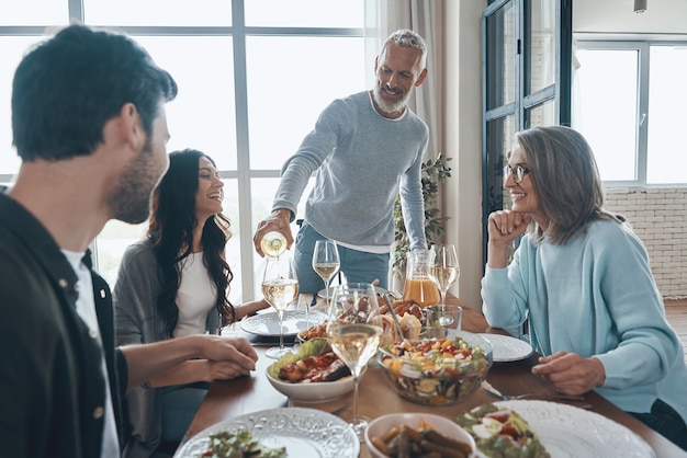 Glücklicher älterer Mann, der Wein brütet und lächelt, während er mit der Familie zu Abend isst?