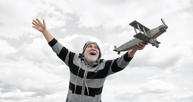 Foto glücklicher älterer mann hoch auf dem himmel hintergrund älterer mann im ruhestand älterer rentner mit spielzeugflugzeug im freien