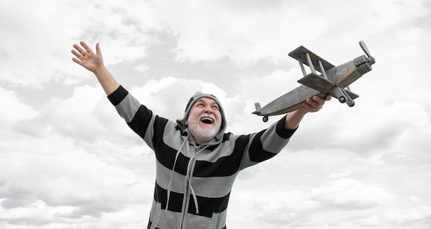 glücklicher älterer Mann hoch auf dem Himmel Hintergrund älterer Mann im Ruhestand älterer Rentner mit Spielzeugflugzeug im Freien