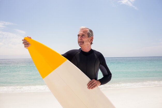 Glücklicher älterer Mann im Wetsuit, der ein Surfbrett hält