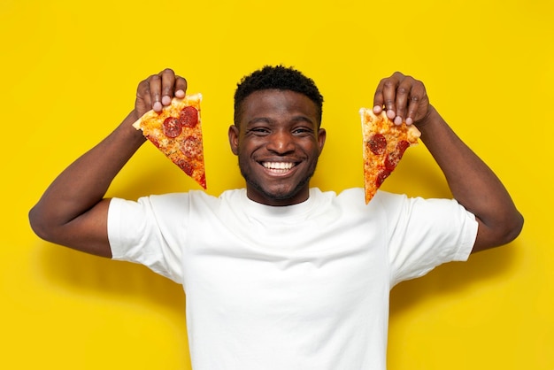 Glücklicher afrikanisch-amerikanischer Mann in weißem T-Shirt, der zwei Stücke Pizza hält und lächelt