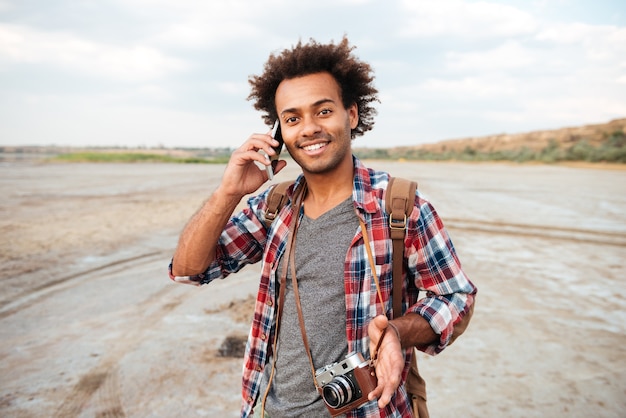 Glücklicher afrikanischer junger Mann mit Vintage-Fotofront, der draußen mit dem Handy spricht