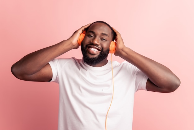 Glücklicher afrikanischer Mann, der Musik mit Kopfhörern anhört, lächeln auf rosa Wand