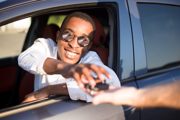 Glücklicher Afroamerikaner in einem Auto mit Schlüssel im Sommer