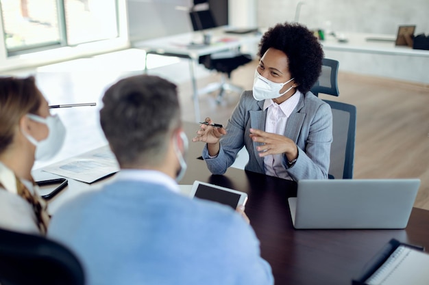 Glücklicher afroamerikanischer Bankmanager mit Gesichtsmaske, der mit einem Paar im Büro spricht