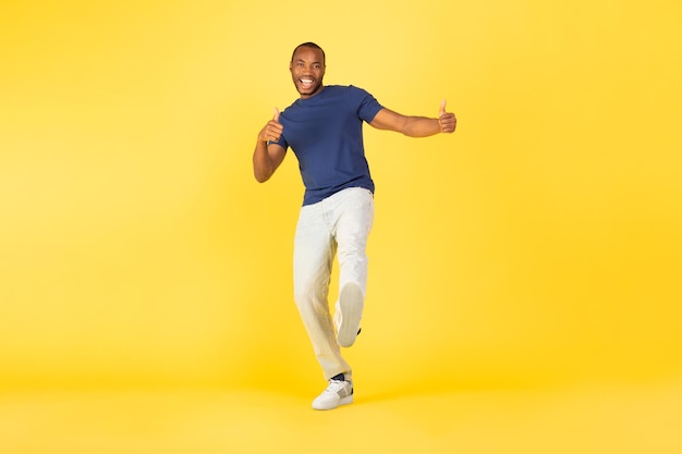Glücklicher afroamerikanischer Mann, der mit dem Daumen nach oben über gelbem Hintergrund gestikuliert