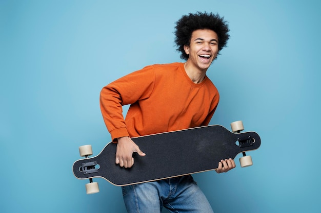 Glücklicher afroamerikanischer Mann mit Longboard simulieren das Gitarrenspiel, isoliert auf blauem Hintergrund