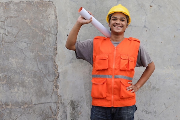 Glücklicher Arbeiter mit Helm und aufgerolltem Bauplan und während der Arbeit am Bauprojekt