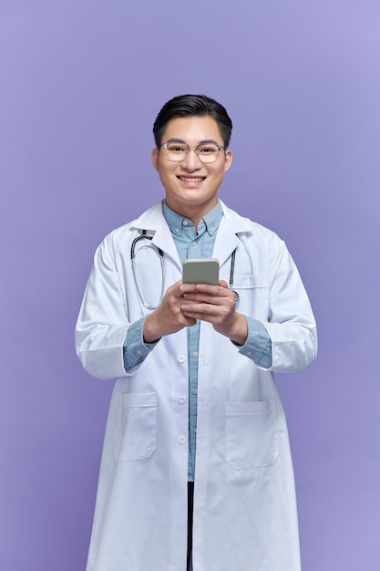 Glücklicher Arzt, der auf einem Smartphone SMS schreibt, isoliert auf violettem Hintergrund