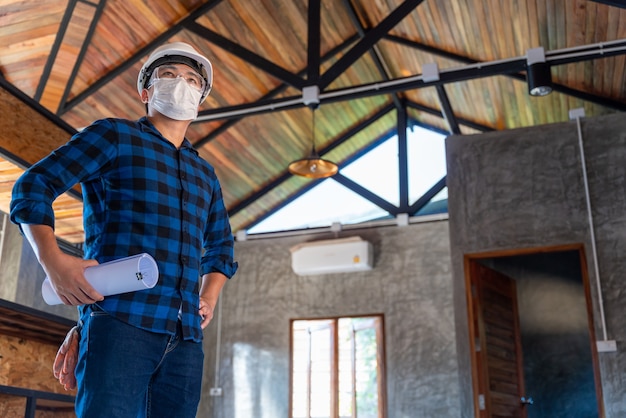 Glücklicher asiatischer Bauingenieur-Techniker nach der Inspektion der Holzstruktur unter dem Dach auf der Baustelle oder der Baustelle eines Hauses.
