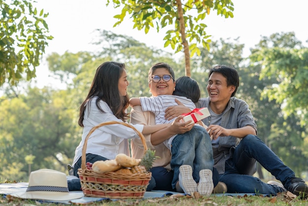 Glücklicher asiatischer Familienenkel, der Großmutter beim Picknicken im Park eine Geschenkbox umarmt und gibt