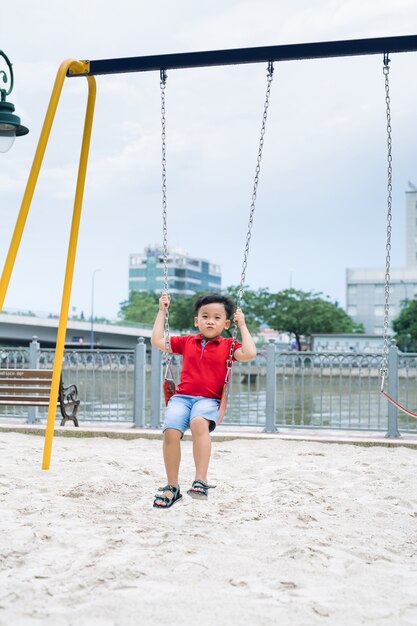 Glücklicher asiatischer Junge, der auf dem Spielplatz im Park schwingt