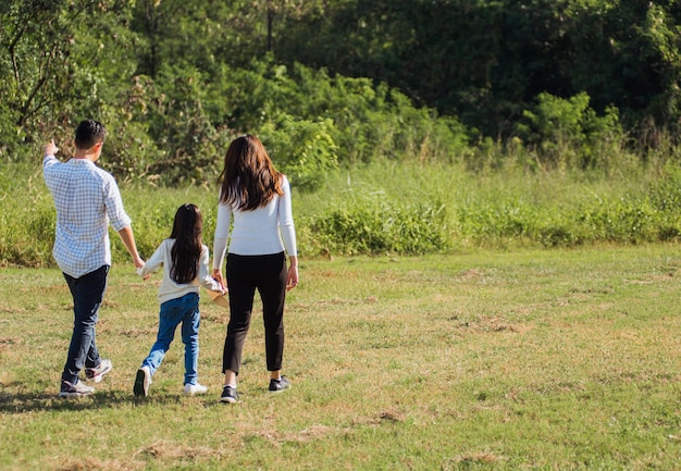Glücklicher asiatischer junger Familienvater, Mutter und Kind, kleines Mädchen, das Spaß hat und an einem sonnigen Sommertag draußen die Straße hinunter im grünen Naturpark spazieren geht