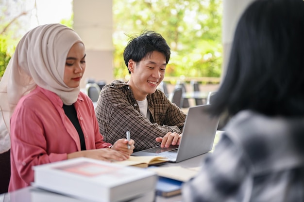 Glücklicher asiatischer männlicher Student, der mit seinen Freunden an einem Gruppenprojekt spricht und arbeitet