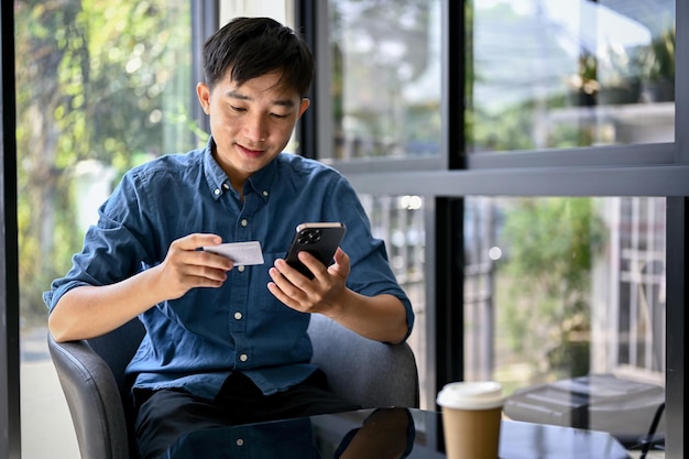 Glücklicher asiatischer Mann, der eine mobile Banking-Anwendung verwendet, um seine Rechnungen online zu bezahlen