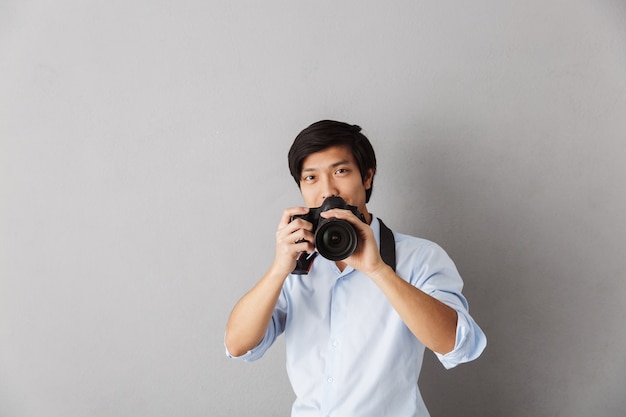 Glücklicher asiatischer Mann, der isoliert steht und ein Foto mit Fotokamera macht