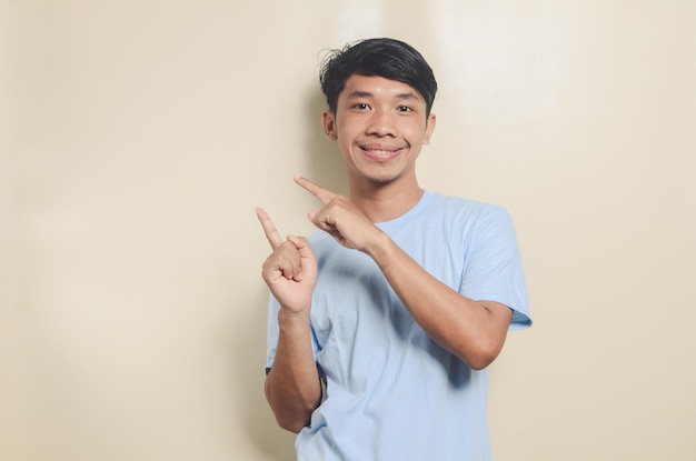 Glücklicher asiatischer Mann mit blauem T-Shirt, der auf leeren Raum auf isoliertem Hintergrund zeigt