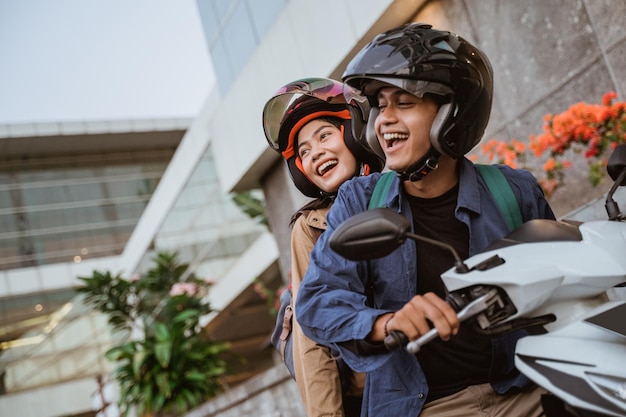 glücklicher asiatischer Mann und Frau, die beim Motorradfahren einen Helm tragen