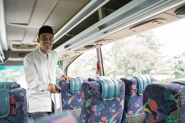Glücklicher asiatischer muslimischer Mann, der eid Mubarak tut, der zurück in seine Heimatstadt reist, indem er einen Bus fährt