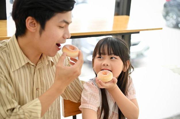 Glücklicher asiatischer Vater isst gerne Donuts mit ihrer süßen kleinen Tochter im Café