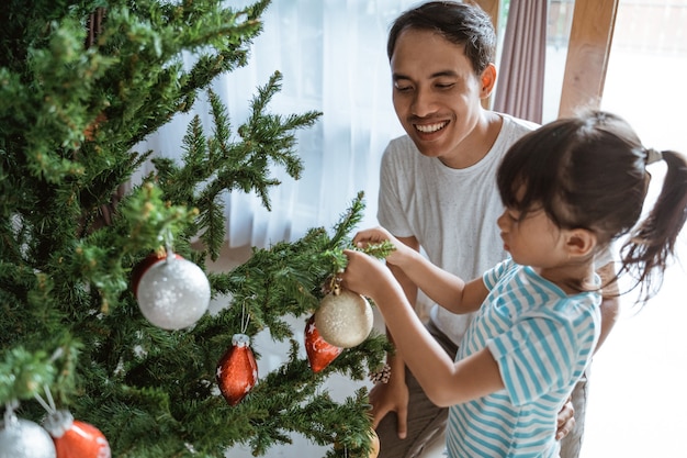 Glücklicher asiatischer Vater und Tochter, die den Weihnachtsbaum schmücken