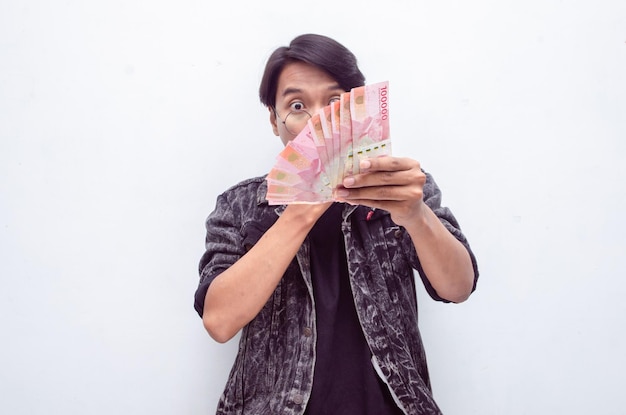 Glücklicher attraktiver indonesischer junger Mann schockiert glücklich, während er Rupiah-Papiergeld hält