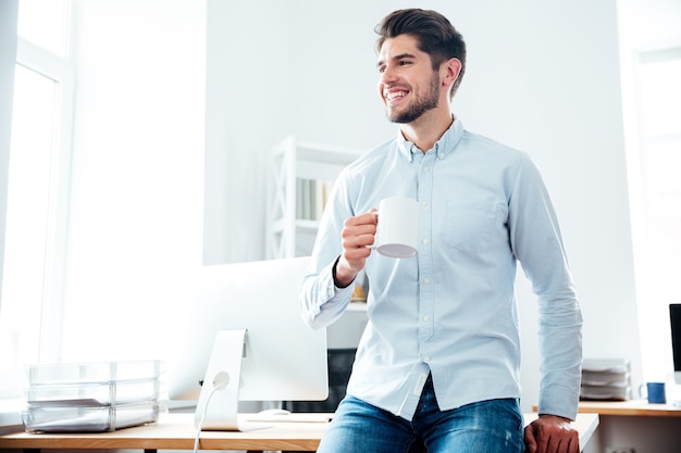 Glücklicher attraktiver junger geschäftsmann, der kaffee im büro trinkt