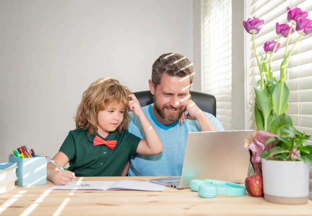 Glücklicher, aufmerksamer Vater und Sohn in der Schule, die online an der Laptop-Kommunikation arbeiten