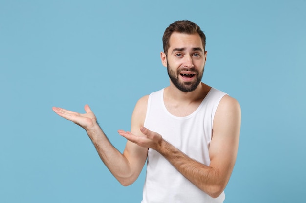 Glücklicher bärtiger junger Mann 20 Jahre alt perfekte Haut mit weißem Hemd isoliert auf blauem pastellfarbenem Wandhintergrund, Studioporträt. Konzept für kosmetische Verfahren im Gesundheitswesen für die Hautpflege. Mock-up-Kopienbereich.