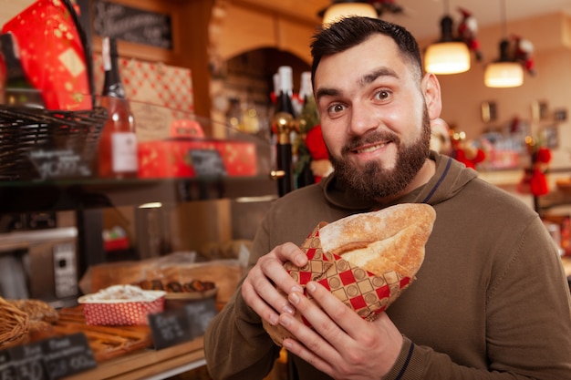 Glücklicher bärtiger Mann, der lustiges aufgeregtes Gesicht beim Einkaufen für köstliches frisches Brot, Kopierraum macht