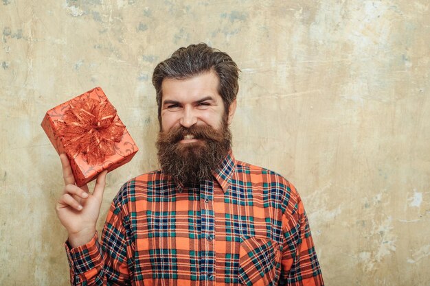 Glücklicher bärtiger Mann, der mit roter Geschenkbox mit Schleife lächelt