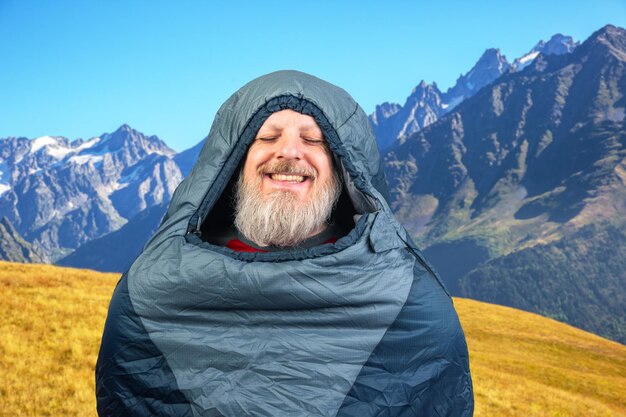 Glücklicher bärtiger Mann in einem Schlafsack vor dem Hintergrund der Natur in der Bergnatur