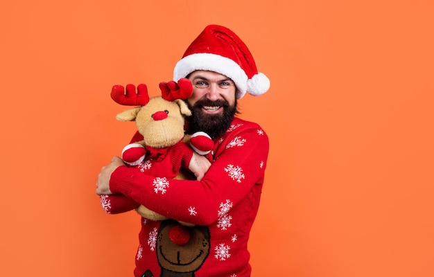 Glücklicher bärtiger Mann in Weihnachtsmannmütze und Strickpullover mit Spielzeug feiern Winterurlaub des neuen Jahres, Weihnachtsgeschenk.