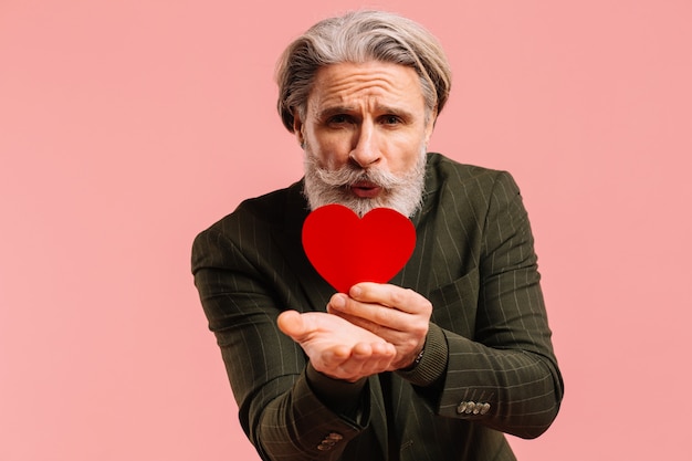 Glücklicher bärtiger und reifer Mann des Schnurrbartes im Khaki-Anzug sendet einen Herzkuss, der Valentine isolierten rosa Hintergrund grüßt.