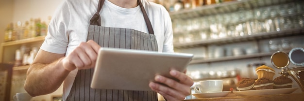 Glücklicher Barista mit digitalem Tablet im Café