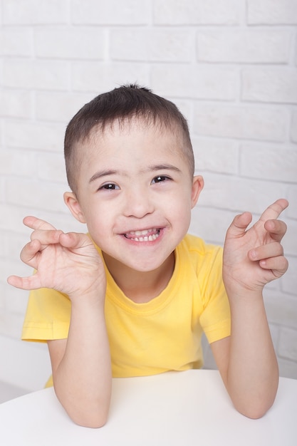 Glücklicher behinderter Junge mit Down-Syndrom lächelnd und winkend an der Kamera, während lokalisiert über weißem Hintergrund. Konzept für Kinder mit Behinderungen und besonderen Bedürfnissen. Web-Banner