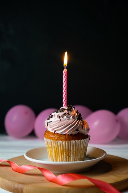 Glücklicher brithday kleiner Kuchen mit einer Kerze auf Schwarzem mit rosa Ballonen