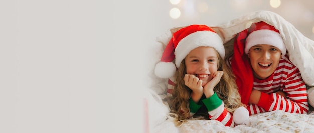 Glücklicher Bruder und Schwester in Neujahrsmützen liegen unter einer Decke in Neujahrspyjamas Weihnachten und Neujahr