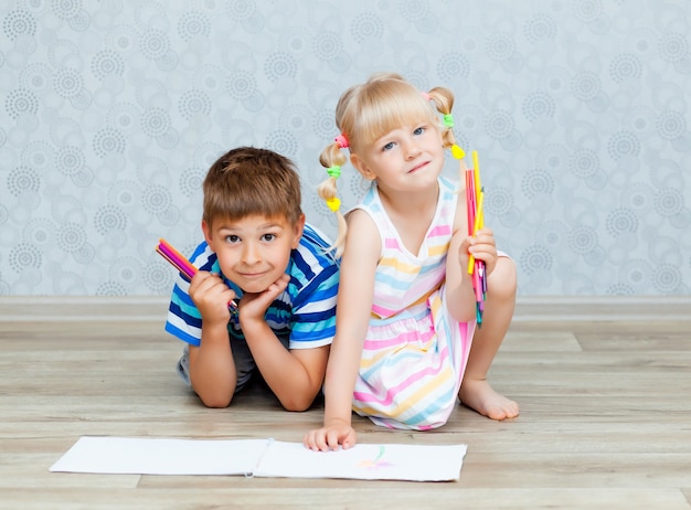 Glücklicher Bruder und Schwester zeichnen, während sie auf dem Wohnzimmerboden liegen. Kinder zeichnen zu Hause mit Bleistiften.