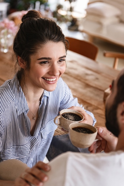 glücklicher brünettes Paar Mann und Frau, die zusammen Kaffee trinken, während sie zu Hause am Tisch sitzen