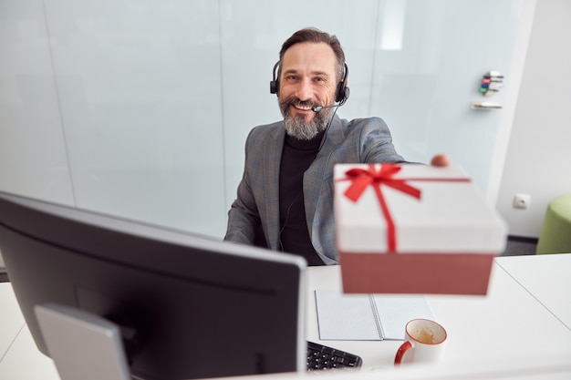 Glücklicher Büroangestellter hält ein Geschenk und lächelt